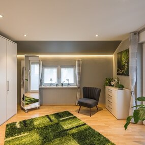 Modern eingerichtetes Schlafzimmer mit großem Kleiderschrank, Sessel und Pflanzen.