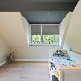 Modernes Kinderzimmer mit Dachschräge, Holzfußboden, Bett und Kuscheltieren am Fenster.