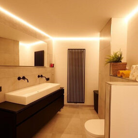 Modernes Badezimmer mit großem Spiegel, LED-Beleuchtung, Waschtisch und Handtuchregal.