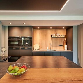 Moderne Küche mit Kochinsel, dunklen Fronten, Holzakzenten und Obstschale im Vordergrund.