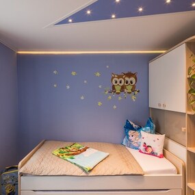 Modernes Kinderzimmer mit blau gestrichener Wand, Eulen-Wandtattoo und gemütlichem Bett.